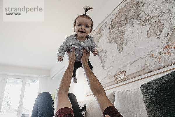 Glückliches Mädchen wird zu Hause im Wohnzimmer von ihrem Vater hochgehoben