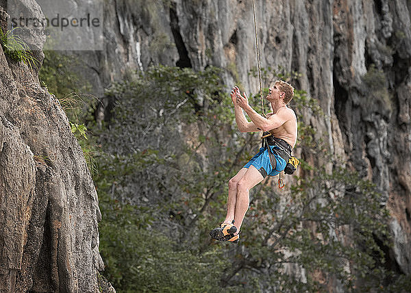 Thailand  Krabi  Lao Liang  barbusiger Bergsteiger  der sich von einer Felswand abseilt
