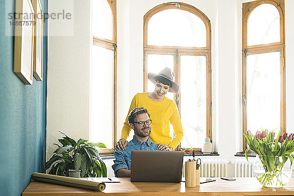 Gelegenheitsunternehmerpaar im Heimbüro  das am Laptop arbeitet und lächelt