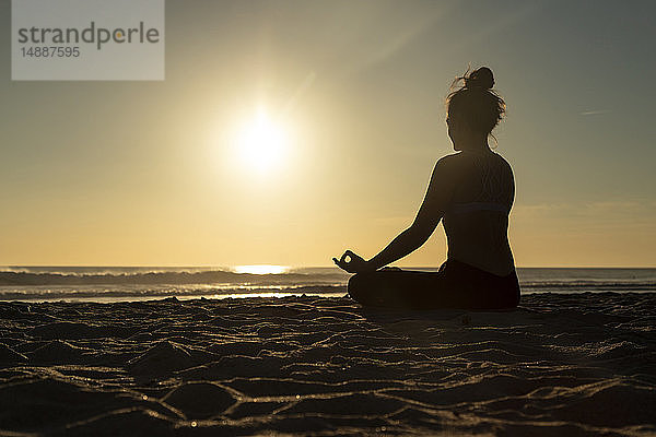 Frau  die am Strand gegen die Abendsonne meditiert