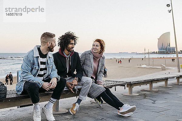 Drei glückliche Freunde sitzen auf einer Bank am Meer