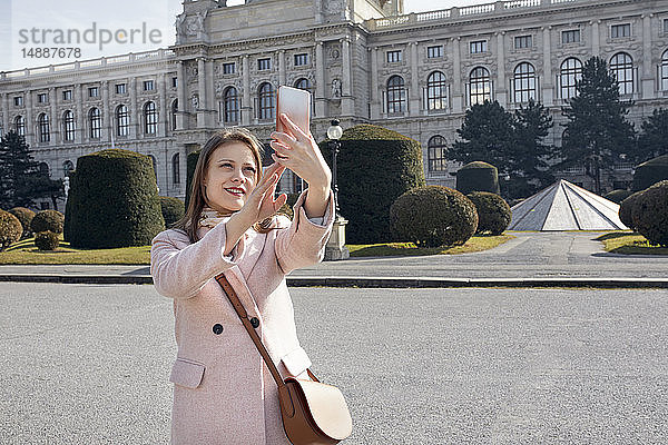 Österreich  Wien  Porträt einer lächelnden jungen Frau  die mit dem Smartphone Selbsthilfe nimmt