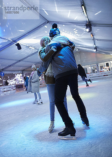 Glückliches junges Paar umarmt sich nachts auf einer Eisbahn