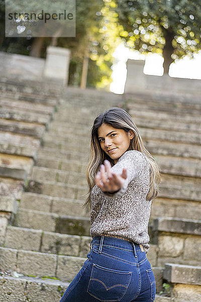 Porträt einer jungen Frau auf einer Treppe  die ihre Hand ausstreckt