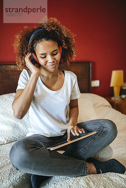 Junge Frau  die mit einer auf dem Bett sitzenden Tafel Musik hört