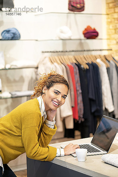 Junge Frau arbeitet in einem Modegeschäft und benutzt einen Laptop