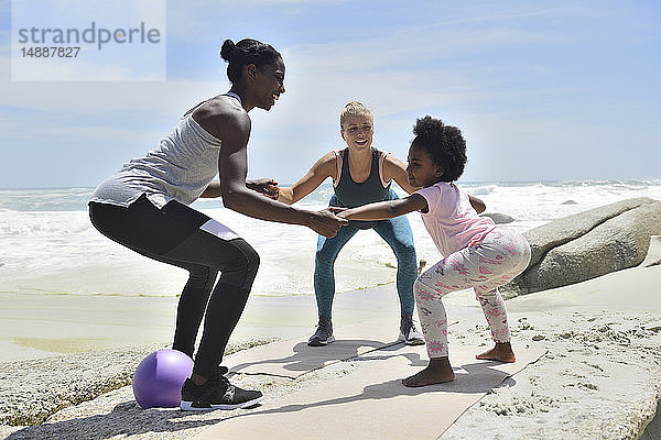 Mutter mit Tochter und Freundin bei einer Fitnessübung am Strand