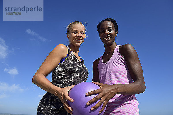 Porträt von zwei lächelnden Frauen  die unter blauem Himmel einen Fitnessball halten