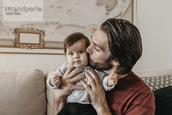 Glücklicher Vater küsst kleines Mädchen zu Hause im Wohnzimmer