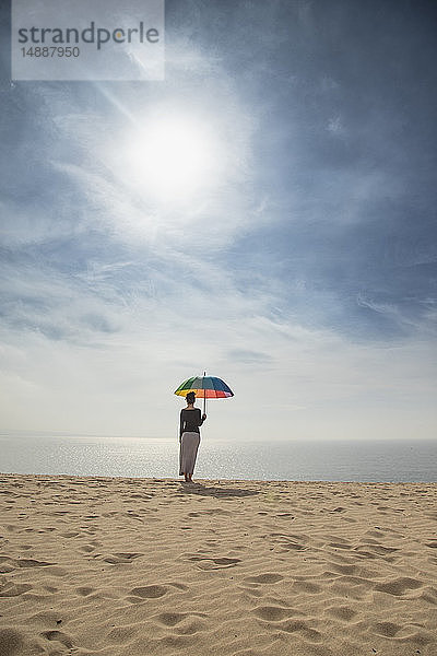 Frau mit buntem Regenschirm am Strand stehend  Rückansicht