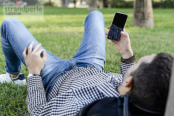 Mann liegt auf Wiese im Stadtpark und benutzt Smartphone