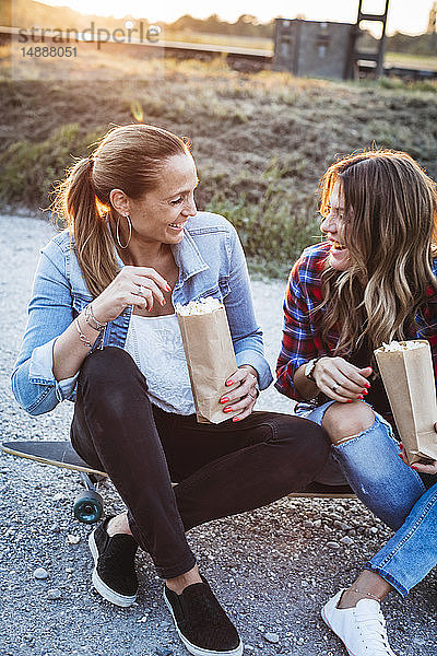 Zwei lachende Freunde sitzen auf dem Longboard und essen Popcorn