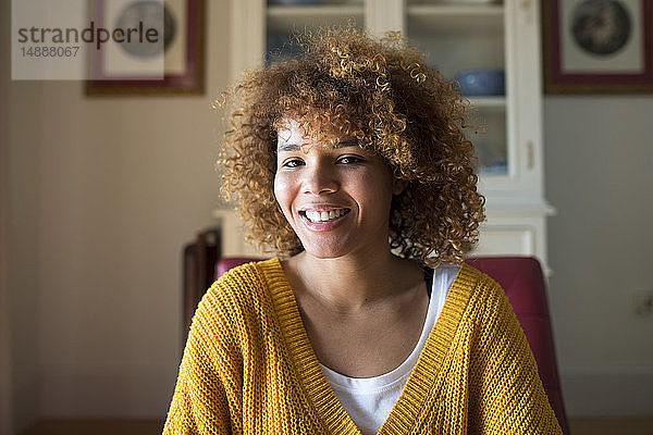 Porträt einer lächelnden jungen Frau mit lockigem Haar zu Hause