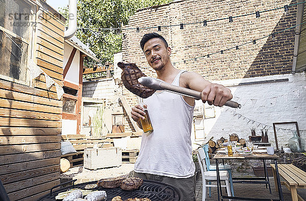Junger Mann bereitet Fleisch auf einem Grill im Hinterhof zu