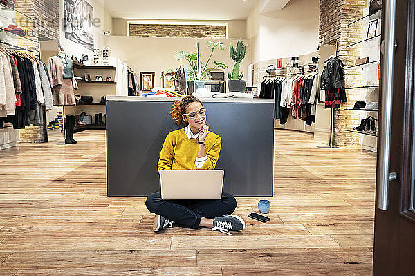 Junge Frau arbeitet in einem Modegeschäft und benutzt einen Laptop