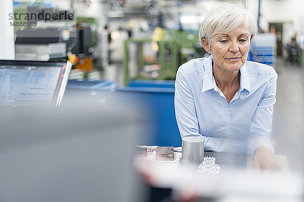 Porträt einer leitenden Geschäftsfrau in einer Fabrik  die ein Werkstück betrachtet