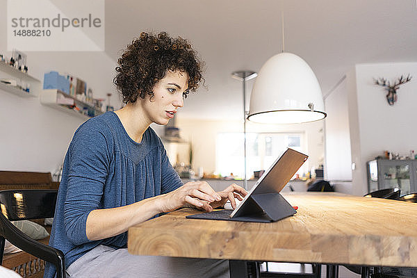 Junge Frau sitzt am Tisch und benutzt ein digitales Tablett
