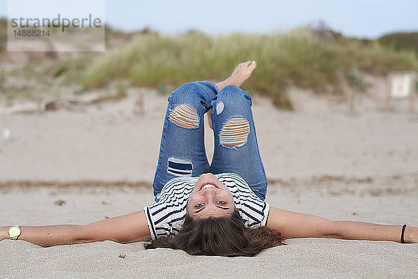 Spanien  Menorca  Porträt einer lächelnden jungen Frau  die auf dem Rücken am Strand liegt