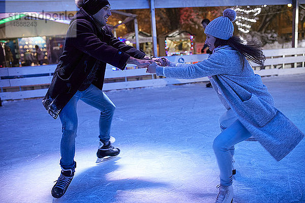 Glückliches junges Paar läuft nachts auf einer Eisbahn Schlittschuh