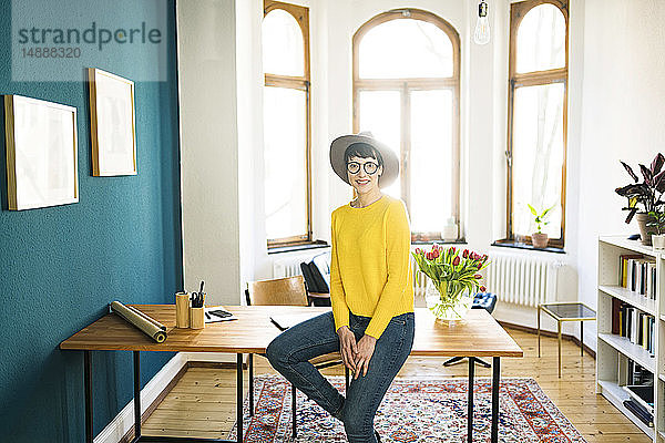 Porträt einer lächelnden Geschäftsfrau im Home Office auf einem Tisch sitzend