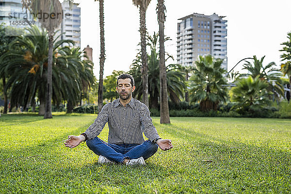 Mann sitzt auf einer Wiese im Stadtpark und macht Yoga-Übungen
