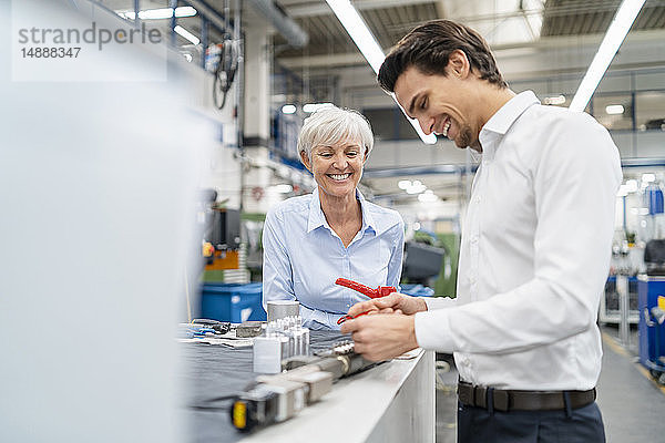 Glücklicher Geschäftsmann und leitende Geschäftsfrau bei der Prüfung eines Werkstücks in einer Fabrik