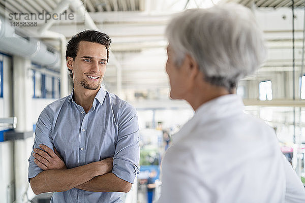 Lächelnder Geschäftsmann im Gespräch mit einer älteren Geschäftsfrau in einer Fabrik