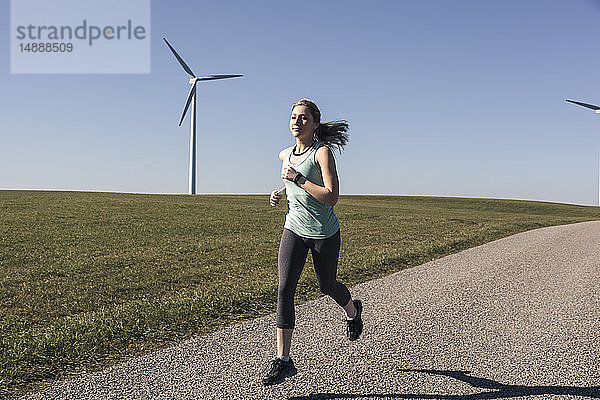 Junge Frau joggt auf dem Feldweg  Windräder im Hintergrund