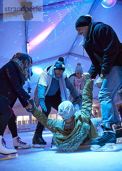 Glückliche Freunde eislaufen auf einer Eisbahn und helfen dem Mann beim Aufstehen