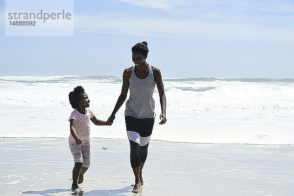 Mutter und Tochter gehen Hand in Hand am Strand