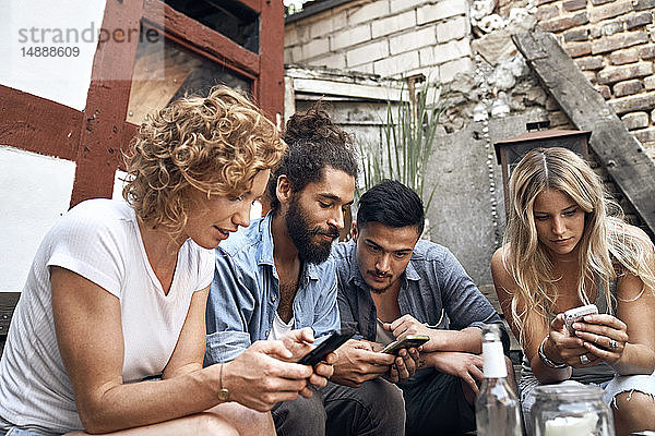 Freunde sitzen in Hinterhöfen und benutzen Smartphones