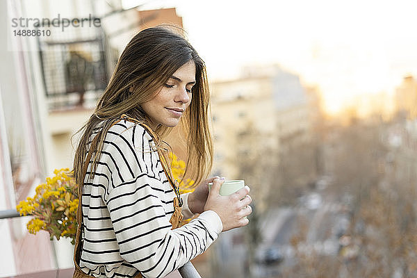 Porträt einer jungen Frau  die sich auf dem Balkon bei einer Tasse Kaffee entspannt