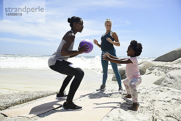 Mutter mit Tochter und Freund trainieren mit einem Ball am Strand