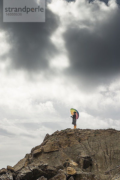 Frau mit buntem Regenschirm auf einem Hügel am Strand stehend