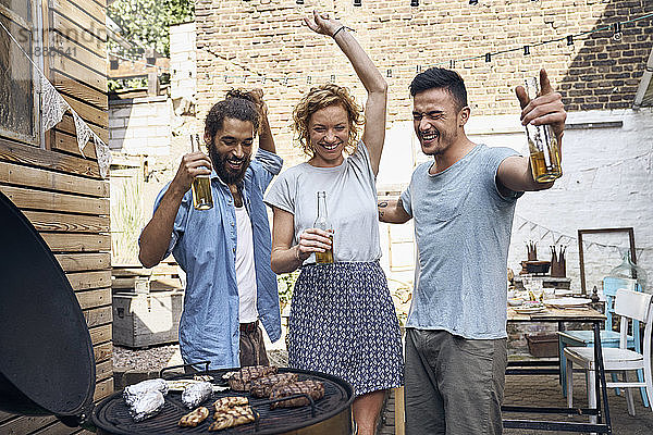 Freunde beim Grillen im Hinterhof  bei der Zubereitung von Fleisch auf dem Grill