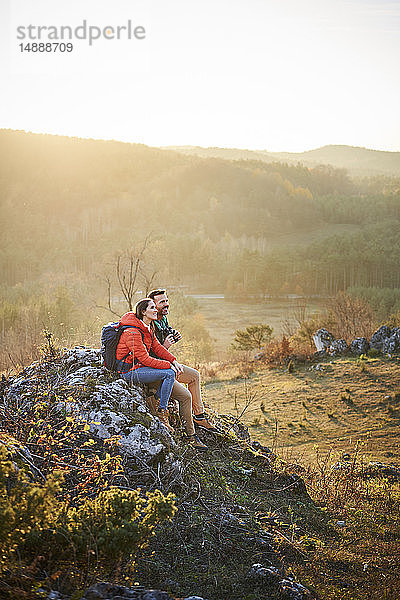 Paar auf einer Wanderung in den Bergen bei einer Pause auf einem Fels sitzend