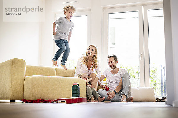 Glückliche Familie zieht in ihr neues Zuhause ein  Junge springt auf die Couch