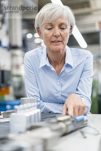 Porträt einer leitenden Geschäftsfrau in einer Fabrik  die ein Werkstück betrachtet