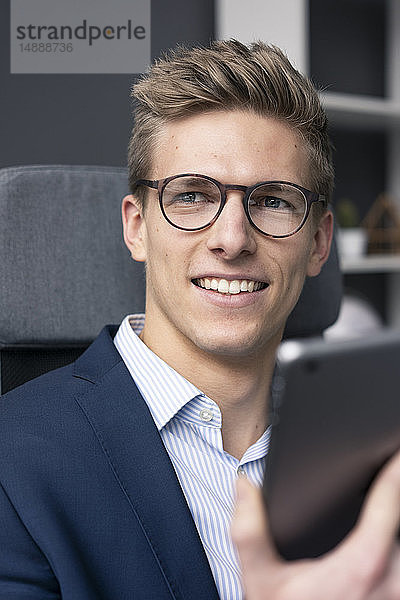 Lächelnder junger Geschäftsmann sitzt auf Bürostuhl mit Tablett