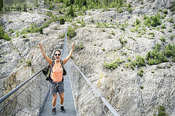 Schweiz  Wallis  jubelnde Frau auf einer Wanderung in den Bergen von der Belalp zur Riederalp auf einer schwingenden Brücke
