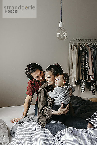 Glückliche Familie mit einem kleinen Mädchen  das zu Hause auf dem Bett sitzt