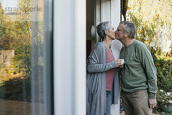 Zärtliches Seniorenpaar küsst sich an der Terrassentür