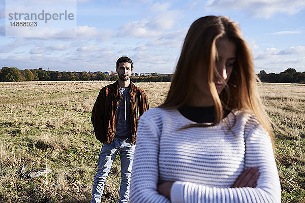 Seriöse junge Frau steht auf einem Feld mit einem Mann hinter ihr