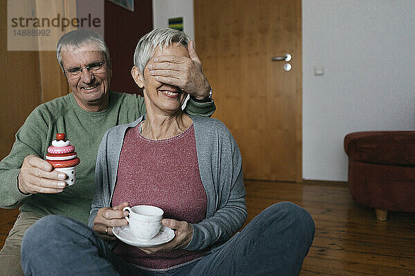 Glückliches älteres Ehepaar sitzt zu Hause auf dem Boden und amüsiert