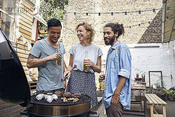 Freunde beim Grillen im Hinterhof  bei der Zubereitung von Fleisch auf dem Grill