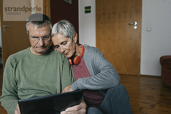 Älteres Ehepaar sitzt zu Hause auf dem Boden und schaut auf die Tablette