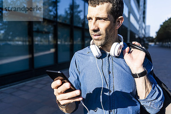 Porträt eines Mannes mit Kopfhörer  Tasche und Mobiltelefon  der in die Ferne schaut