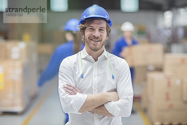 Porträt eines lächelnden Mannes mit Schutzhelm in einer Fabrik