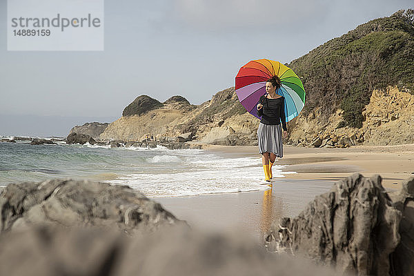 Frau mit buntem Sonnenschirm am Strand spazieren