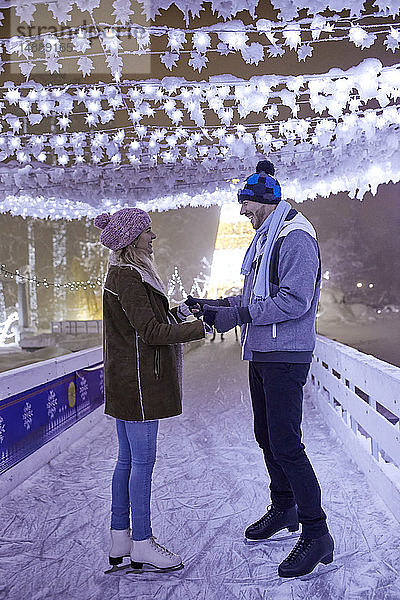 Glückliches junges Paar auf einer Eislaufbahn bei Nacht